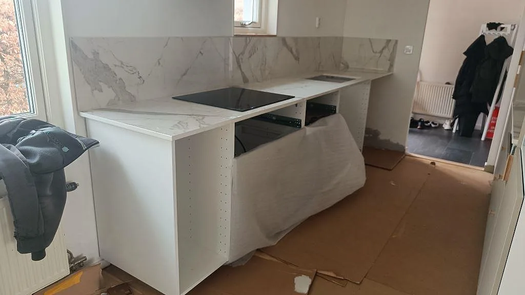 Köksbänkskiva i polerad Dekton Vigil, vit keramik med grå ådring, svart häll och matchande stänkskydd i Smygehamn.