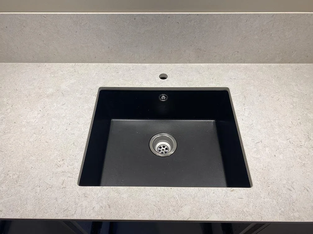 Närbild av svart diskho i matt Dekton VK01 Nebbia med tapputtag och matchande stänkskydd i ett kök i Älmhult.