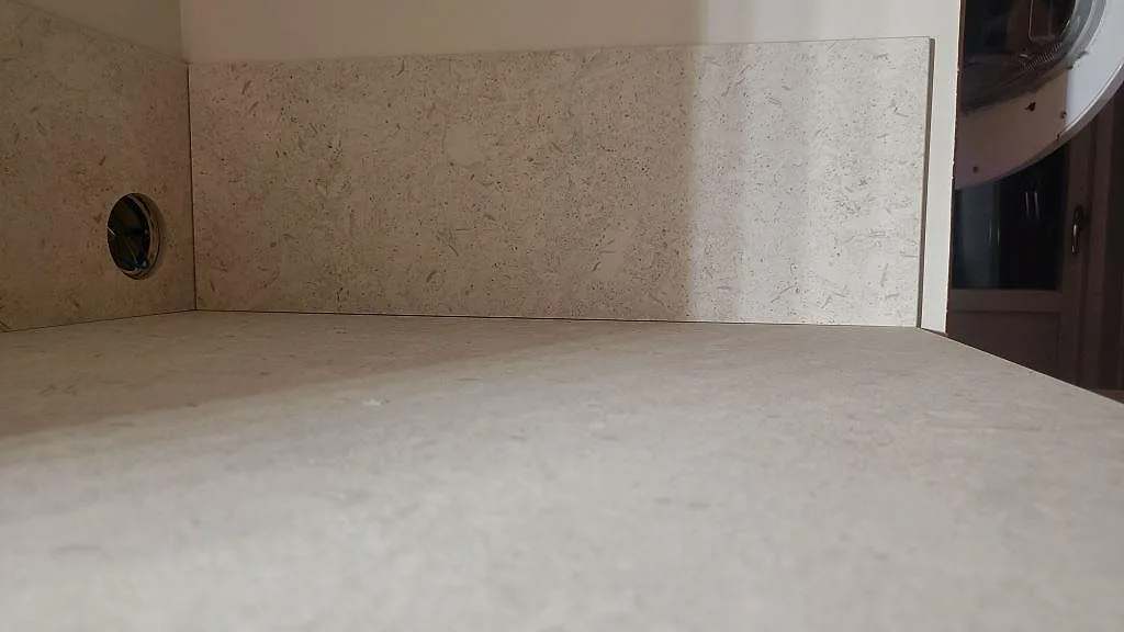Närbild av matt Dekton VK01 Nebbia med matchande stänkskydd och kabelgenomföring över bänkskivan i Asarum.