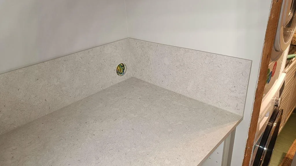 Installerad köksbänkskiva i matt Dekton VK01 Nebbia med stänkskydd runt hörn och ljus väggyta i Asarum.
