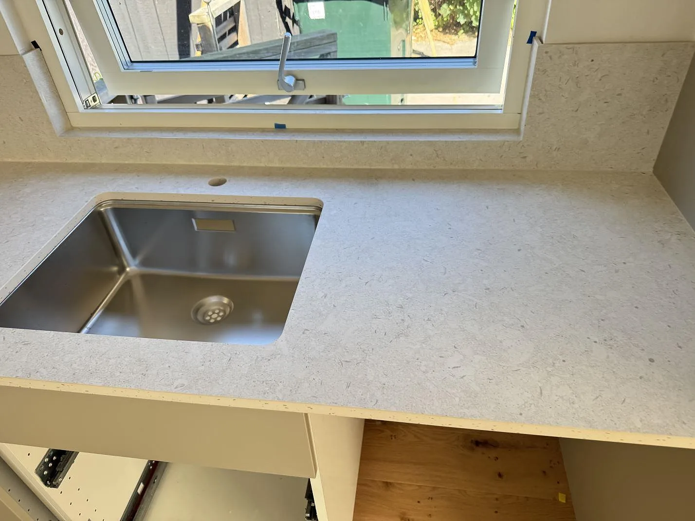 Köksbänkskiva i matt Dekton VK01 Nebbia keramik med rostfri diskho och låg stänkskyddsyta under fönster i Bjärred.