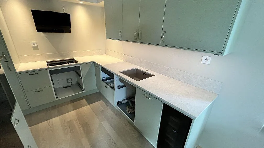 L-formad köksbänkskiva i matt Dekton VK01 Nebbia med häll under fläkt och diskzon i ett grönt kök i Bromma.
