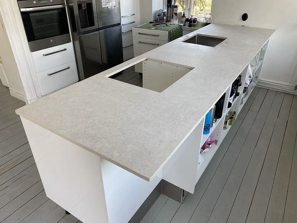Köksbänkskiva i matt Dekton VK01 Nebbia, ljus keramik med diskho och större ursåg i ett kök under montering i Eslöv.