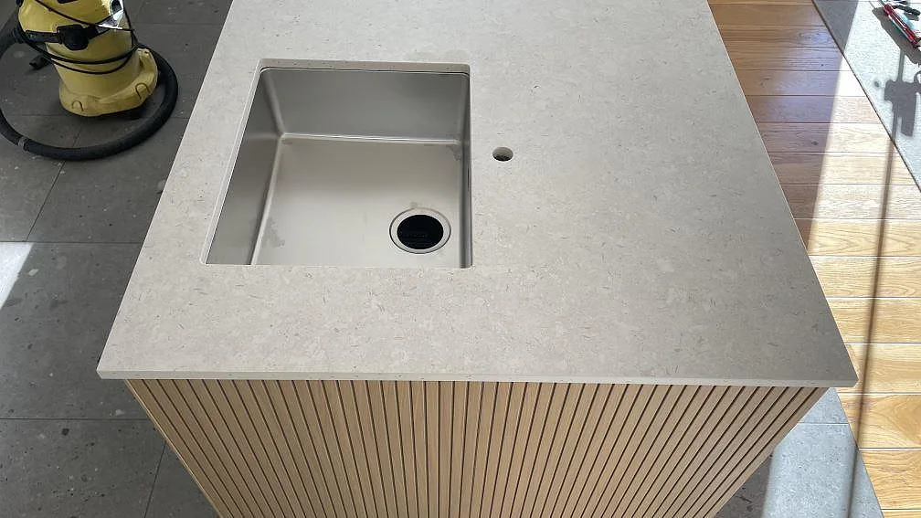 Detalj av matt köksbänkskiva i Dekton VK01 Nebbia med rostfri diskho, kranhål och ribbad träfront i Helsingborg.