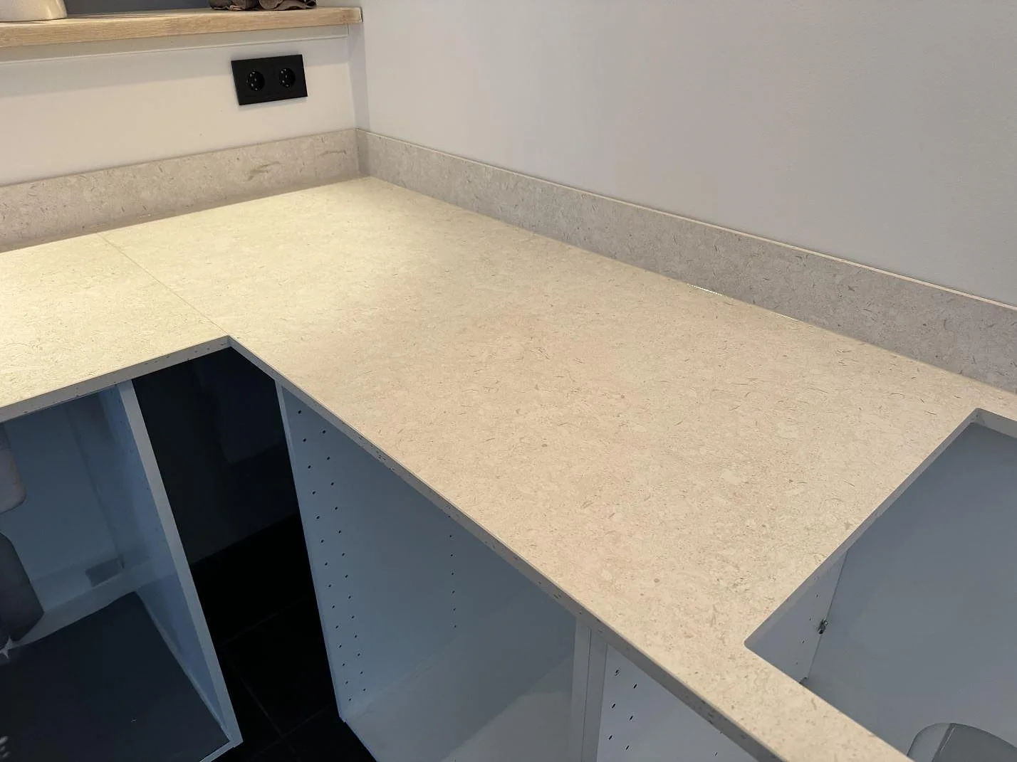 Köksbänkskiva i beige Dekton VK01 Nebbia keramik, matt, med hällöppning och vit köksinredning under montering i Höllviken.