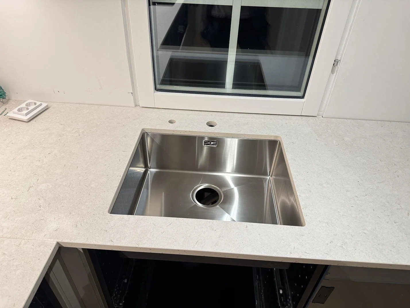 Bänkskiva i matt Dekton VK01 Nebbia keramik vid fönster med rostfri diskho och runda hål bakom i Höllviken.