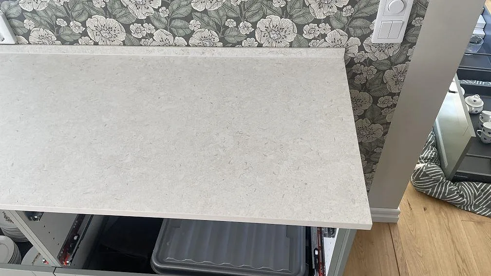 Detalj av hörn och låg stänkkant på matt köksbänkskiva i Dekton VK01 Nebbia i Hörby.