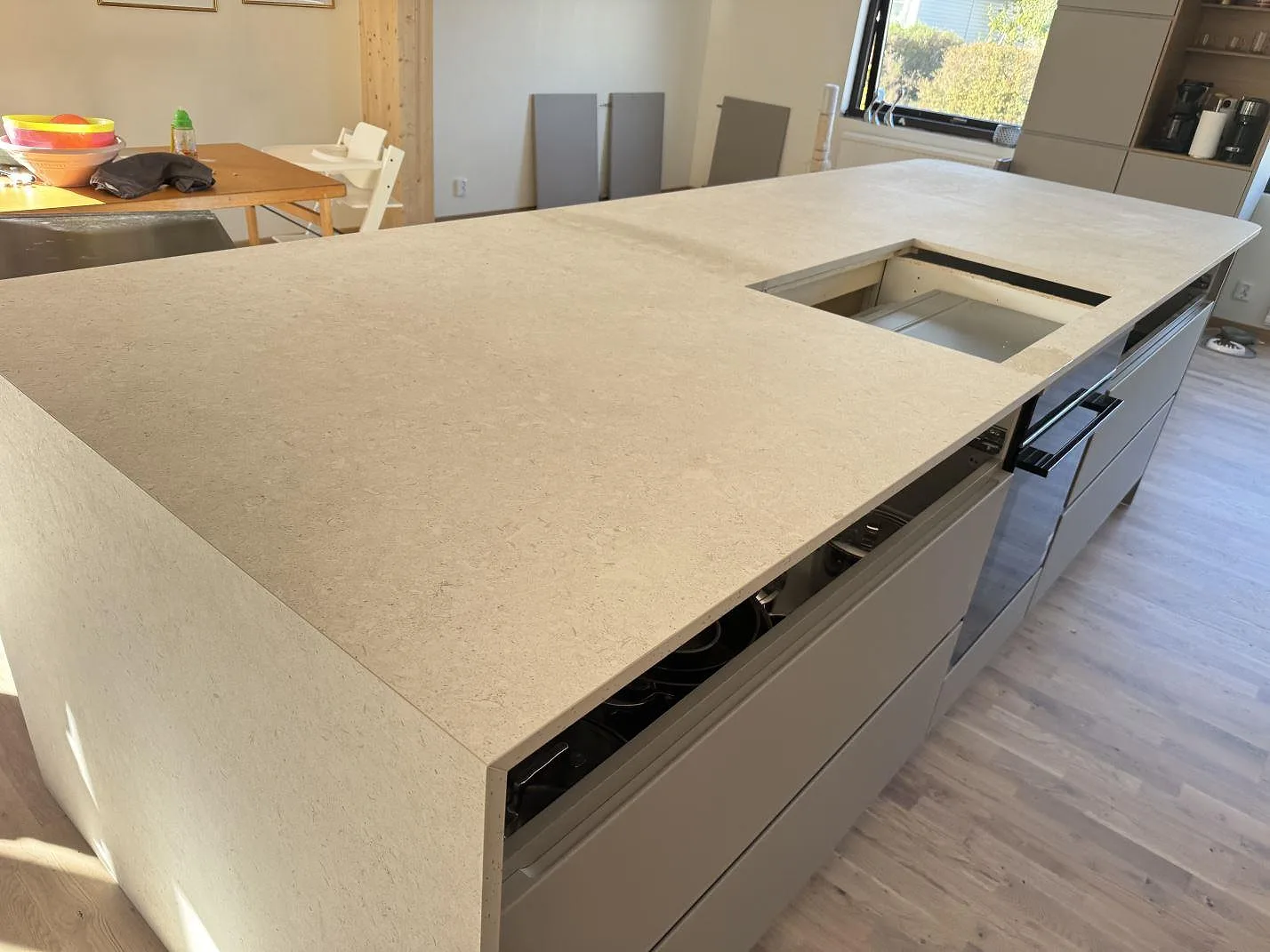 Stor köksö i matt Dekton VK01 Nebbia med ljus stenstruktur och rektangulär öppning under montering i Löddeköpinge.