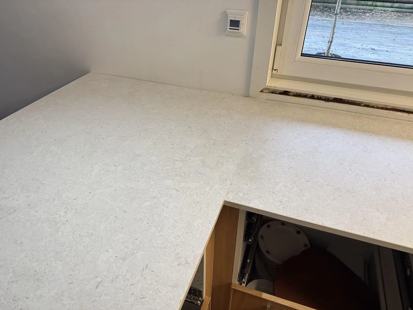 Ljus köksbänkskiva i 20 mm matt Dekton VK01 Nebbia vid fönster och öppna köksstommar i Löddeköpinge.