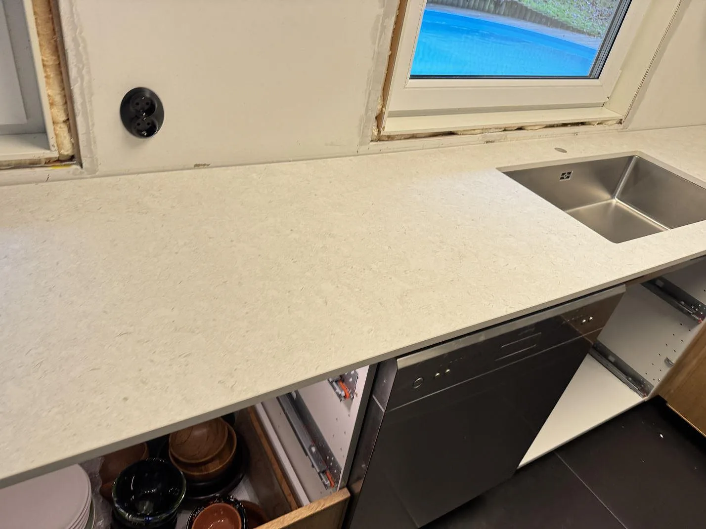 Matt köksbänkskiva i Dekton VK01 Nebbia med rostfri diskho och fönsterljus i ett kök i Löddeköpinge.