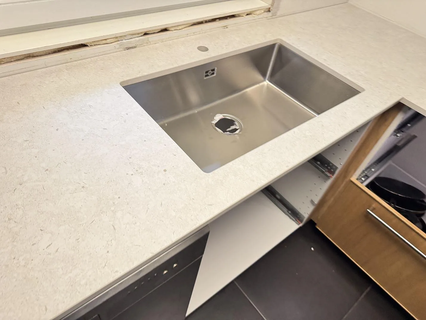 Närbild på rostfri diskho i en ljus köksbänkskiva av matt Dekton VK01 Nebbia i Löddeköpinge.