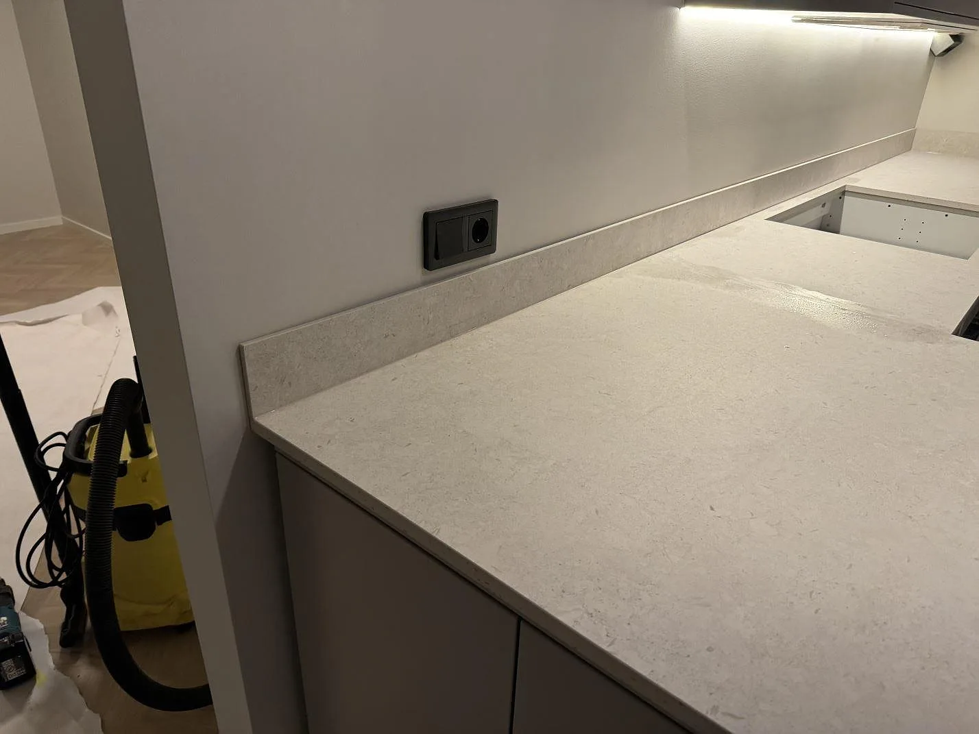 Närbild på matt Dekton VK01 Nebbia som köksbänkskiva med lågt stänkskydd och vägguttag i Trelleborg.