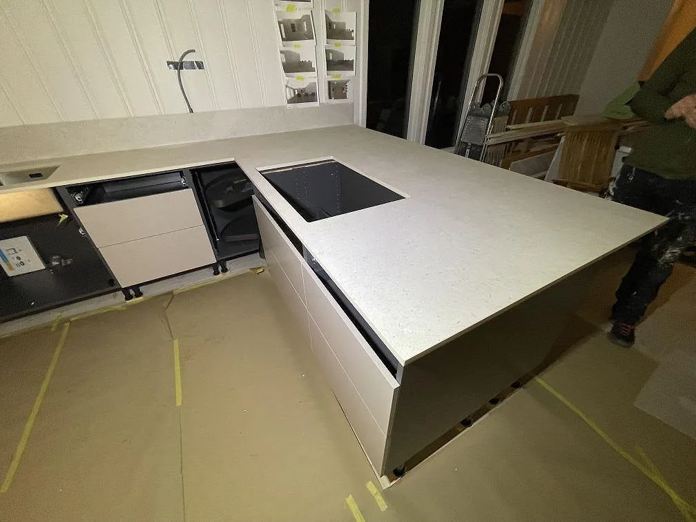 Köksö i matt Dekton VK01 Nebbia med infälld svart induktionshäll och tjock framkant i ett kök i Trosa.