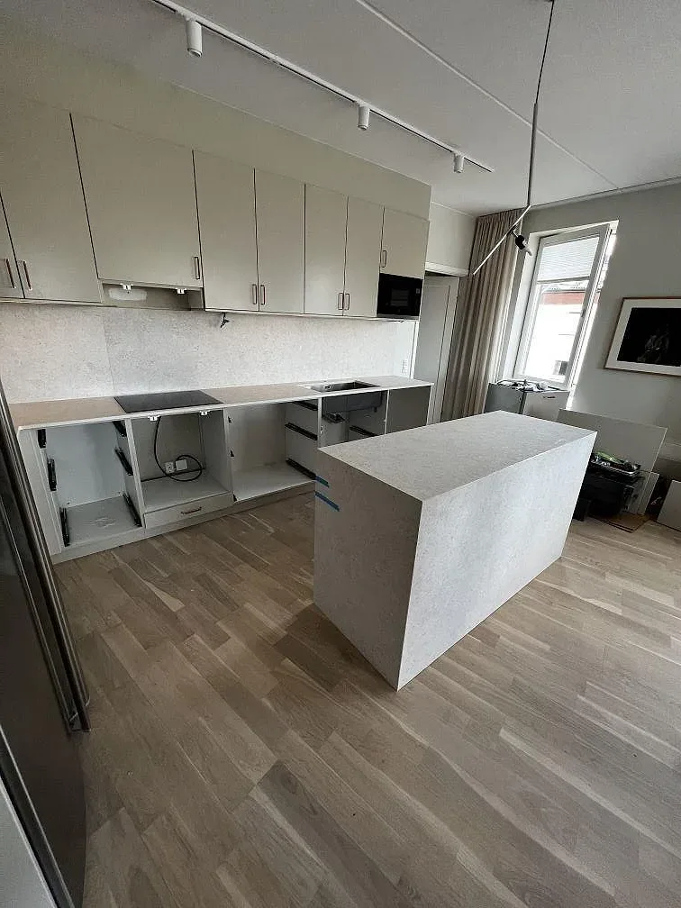 Köksö i ljusgrå Dekton VK01 Nebbia keramik, matt, med matchande bänkskiva längs väggen i Värnamo.