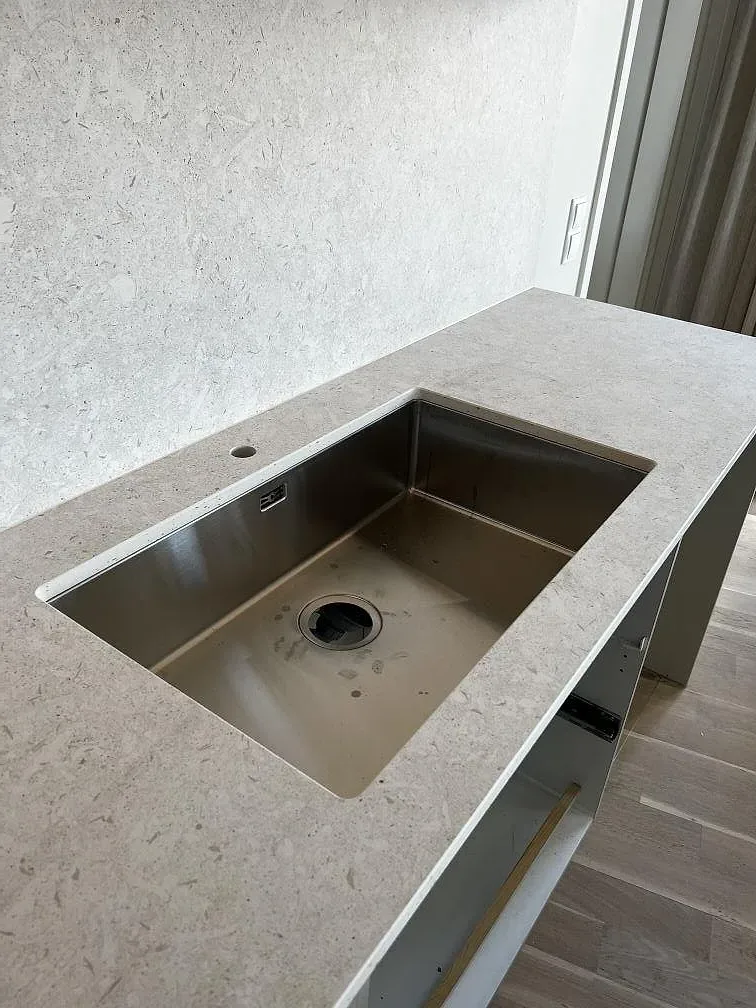 Underlimmad rostfri diskho i matt Dekton VK01 Nebbia keramik på köksö under montering i Värnamo.