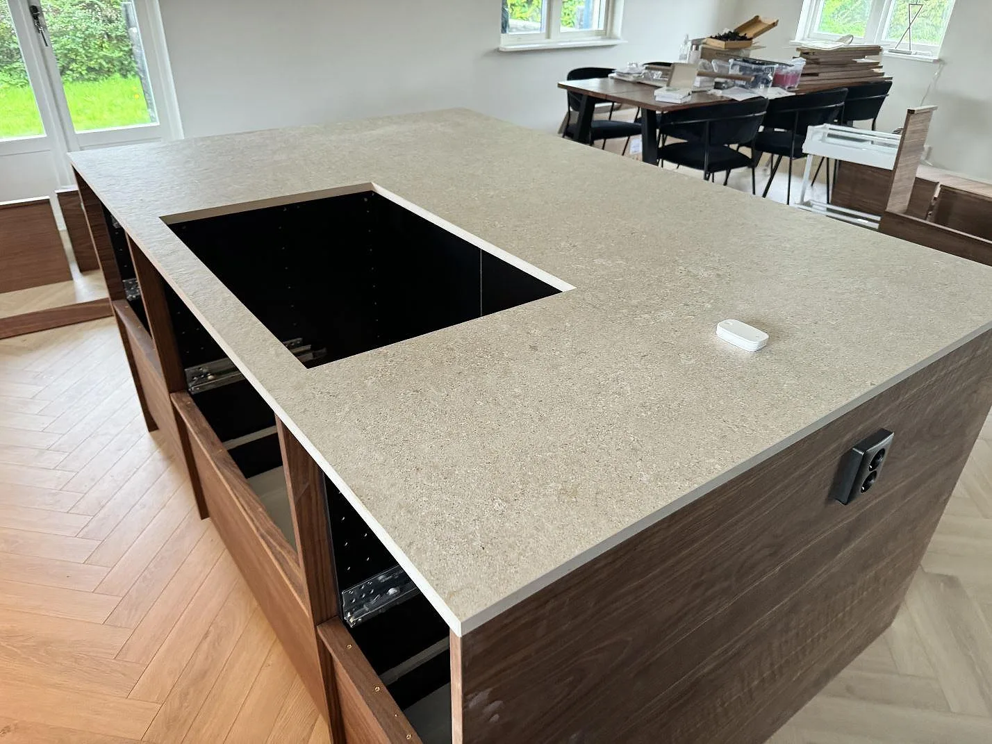 Köksö med bänkskiva i matt keramisk Dekton Vk02 Avorio och hällöppning på valnötsfärgad bas i ett kök i Färlöv.
