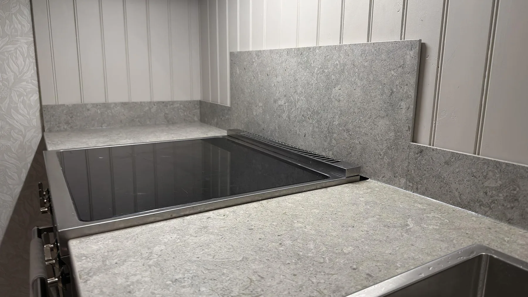 Induktionshäll nedfälld i en matt grå Dekton VK03 Grigio bänkskiva med uppvikt stänkkant i samma keramik i ett kök i Charlottenberg.