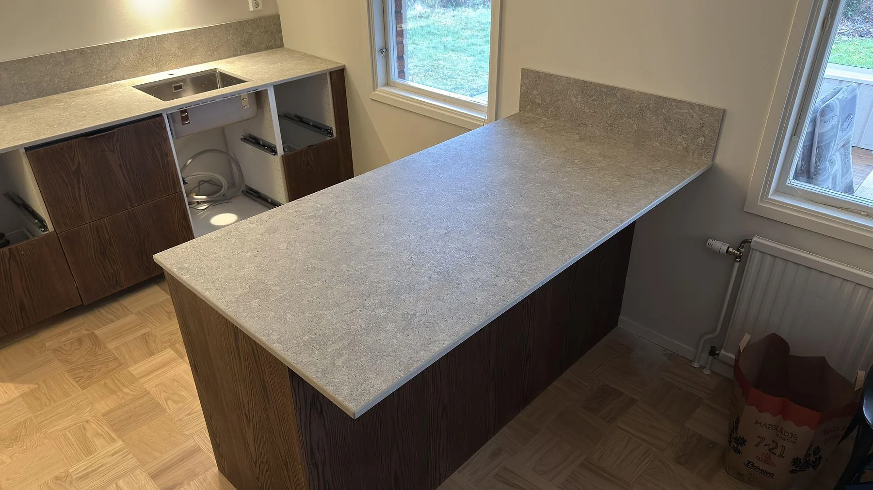 Köksö i matt Dekton VK03 Grigio med lång grå keramikyta och diskbänksrad bakom i Eskilstuna.