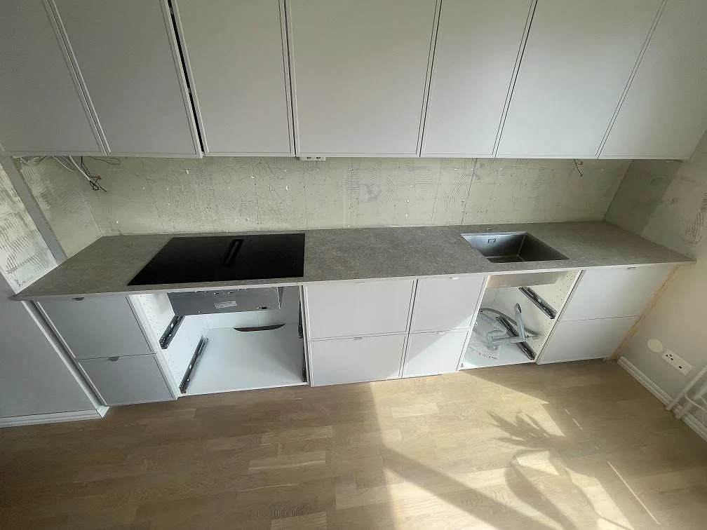 Köksbänkskiva i grå Dekton VK03 Grigio, matt keramik, med svart induktionshäll och rostfri diskho i ett kök i Järfälla.