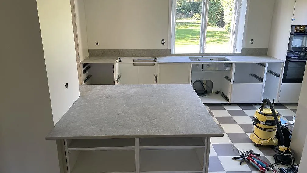Köksbänkskiva i matt grå Dekton VK03 Grigio med köksö, väggbänkar och låg stänkkant i ett kök i Kävlinge.