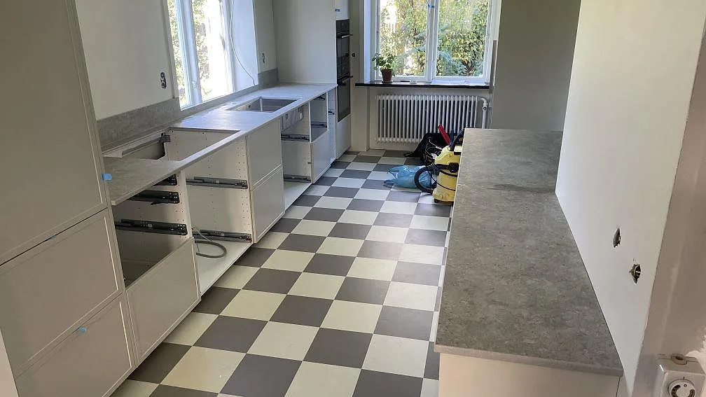 Lång väggbänk och sidobänk i matt Dekton VK03 Grigio under montering i ett kök i Kävlinge.