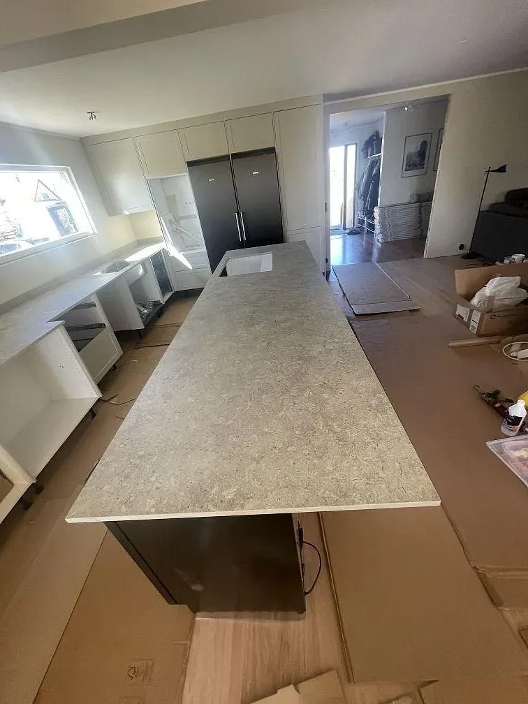 Lång köksö i grå Dekton VK03 Grigio, matt, sedd längs köket med köksstommar och fönster i bakgrunden i Kristianstad.