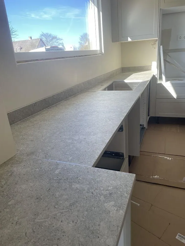 Vinklad bänkrad i grå Dekton VK03 Grigio, matt, med förberett undermonterat urtag för diskho vid fönstret i ett kök i Kristianstad.