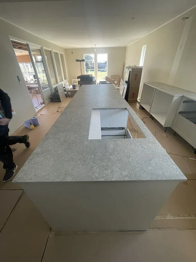 Köksö med waterfall-kant i grå marmorlik Dekton VK03 Grigio, matt, med förberett urtag i ytan, i ett kök i Kristianstad.