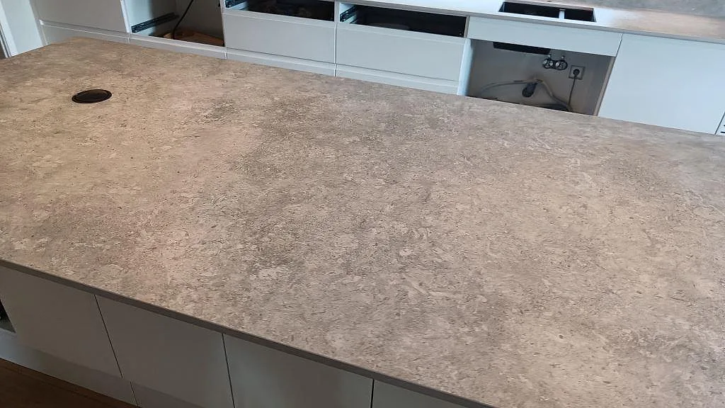 Installerad köksö i Dekton VK03 Grigio, matt keramik, med rund kabelgenomföring och vit köksinredning i Kullavik.