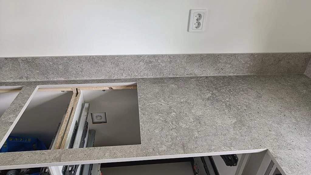 Installerad köksbänkskiva i Dekton VK03 Grigio, matt grå keramik, med stänkkant och öppna skåpstommar i Malmö.