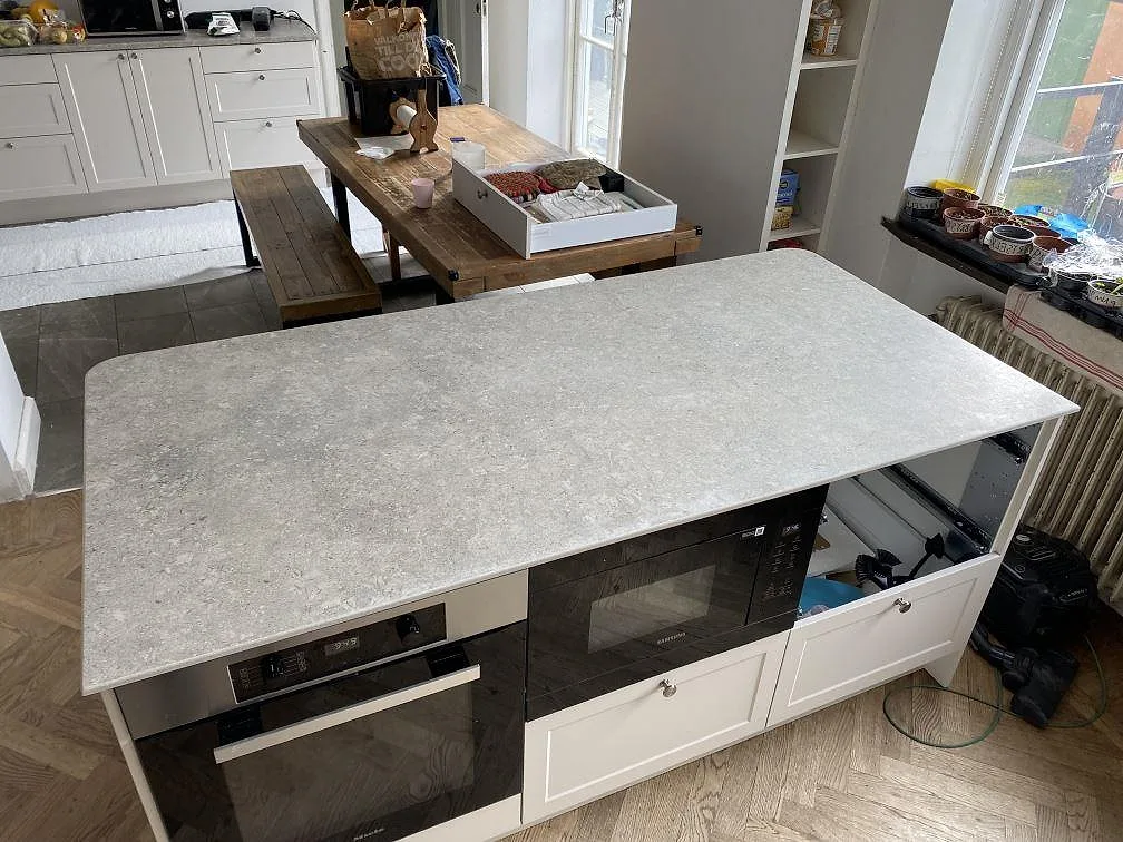 Stor köksö med köksbänkskiva i matt grå Dekton VK03 Grigio, sintrad keramik, över vita skåp i ett kök i Malmö.