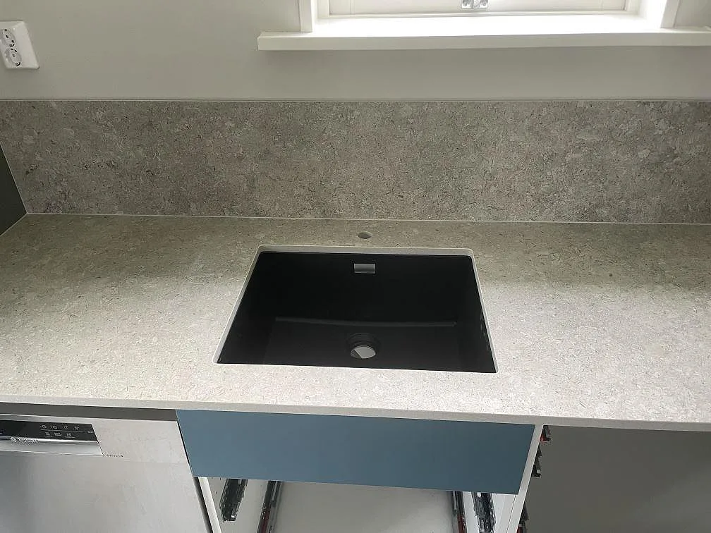 Keramisk köksbänkskiva i matt Dekton VK03 Grigio med svart diskho och stänkskydd vid fönster i Stora Skedvi.