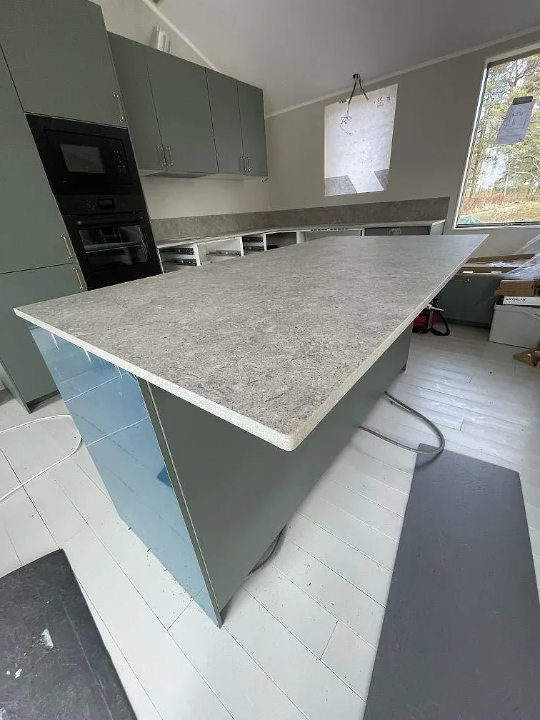 Köksö i Dekton VK03 Grigio med synlig gavelklädsel och matt yta, salviagröna skåp och svart inbyggd ugn i ett kök i Värmdö.