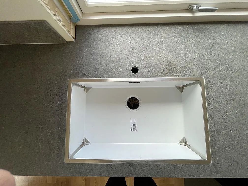 Underlimmad rostfri diskho i matt grafitgrå Dekton VK04 Grafite köksbänkskiva under ett fönster i Hägersten.