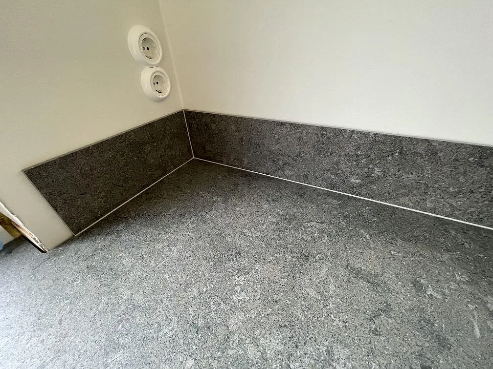 Uppvikt stänkskydd i mörk grafitgrå Dekton VK04 Grafite mot köksbänkskivan i samma matta sten i ett kök i Hägersten.