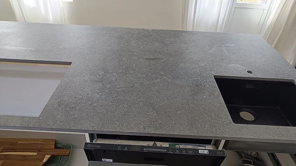 Köksbänkskiva i matt Dekton Vk04 Grafite med svart ho, rund öppning och grå stenstruktur i Höllviken.