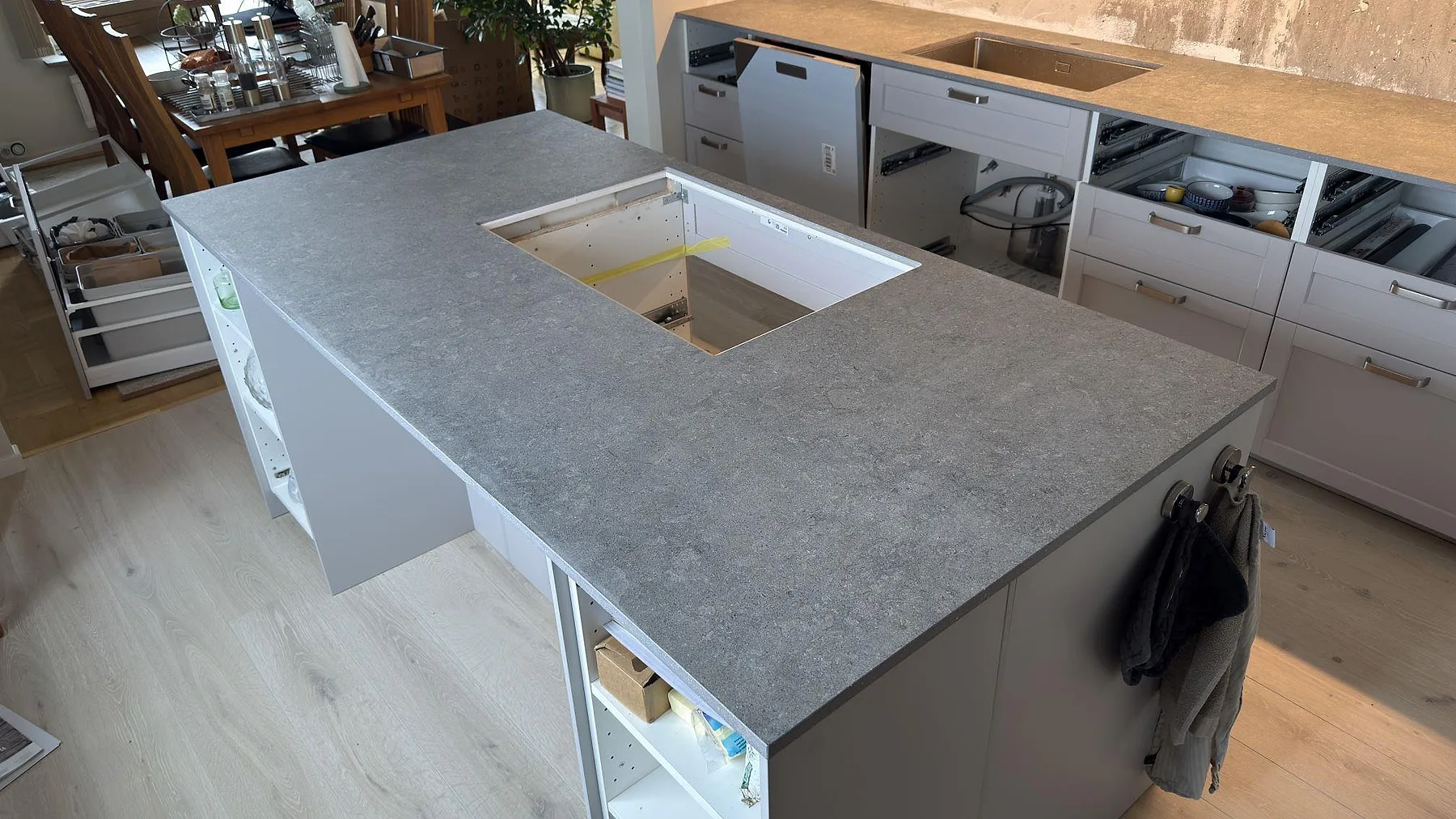 Stor köksö med matt Dekton Vk04 Grafite, grå keramisk bänkskiva och synligt hälluttag under köksmontering i Lidingö.
