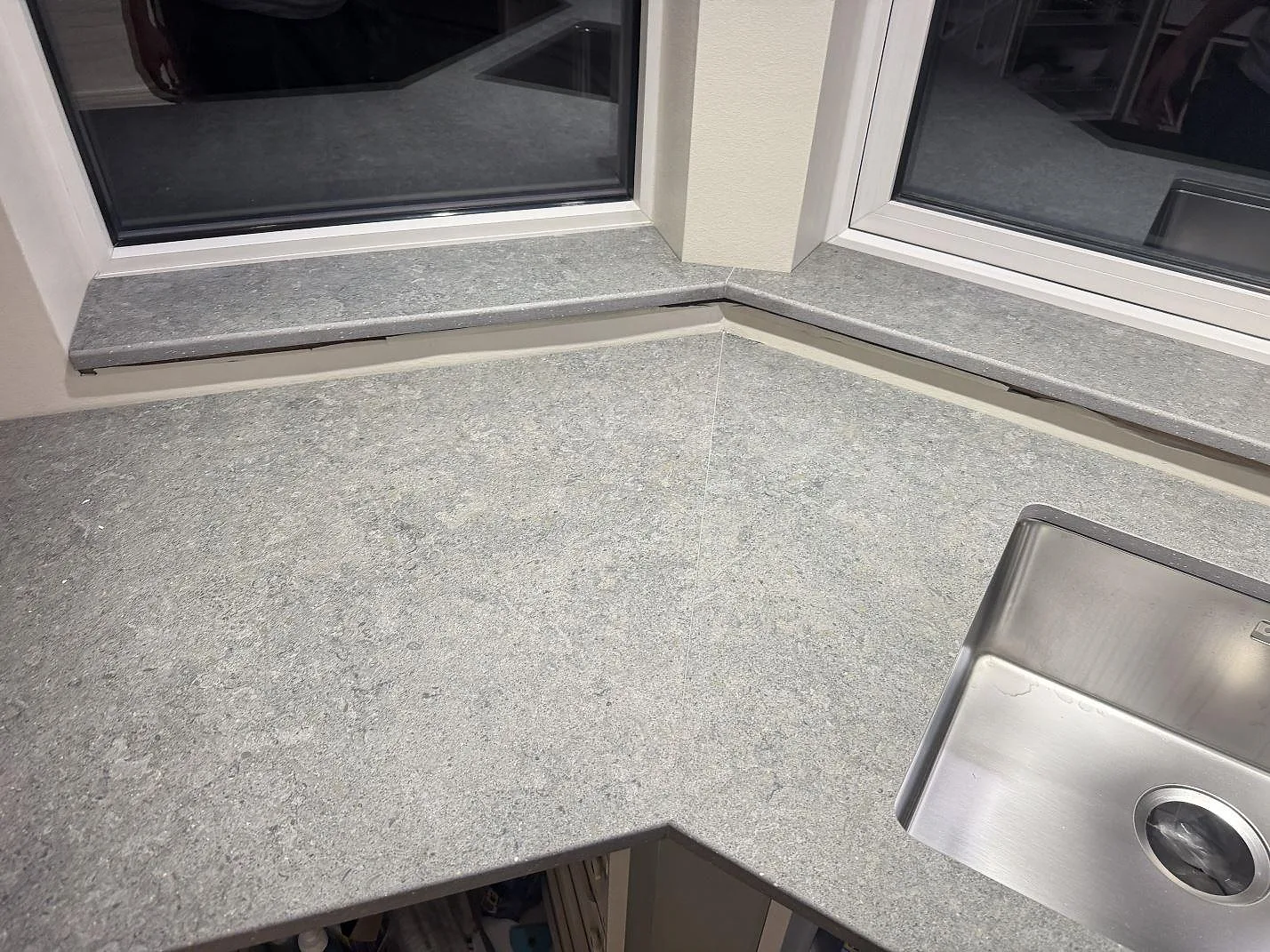 Grå köksbänkskiva i Dekton Vk04 Grafite med synlig stenstruktur och rostfri diskho vid fönster i Ølsted.