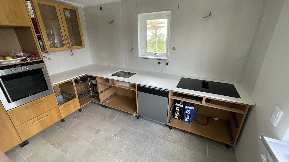 Köksbänkskiva i matt Dekton Zenith, ljus keramik, med rostfri diskho och svart häll i ett kök under montering i Höör.