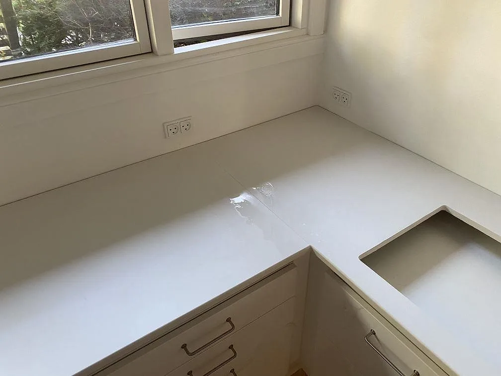 Hörnparti med matt vit Dekton Zenith köksbänkskiva och rektangulär hällöppning i ett kök i Holte.
