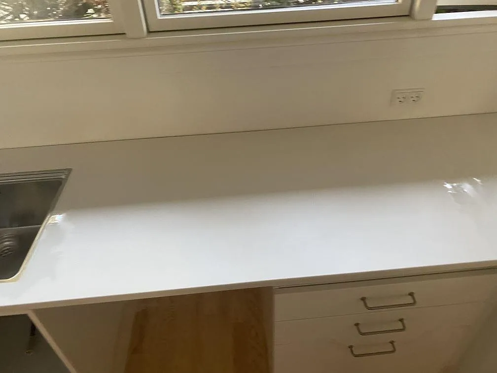 Lång arbetsyta i matt vit Dekton Zenith vid fönstervägg med rostfri diskho i kanten i Holte.