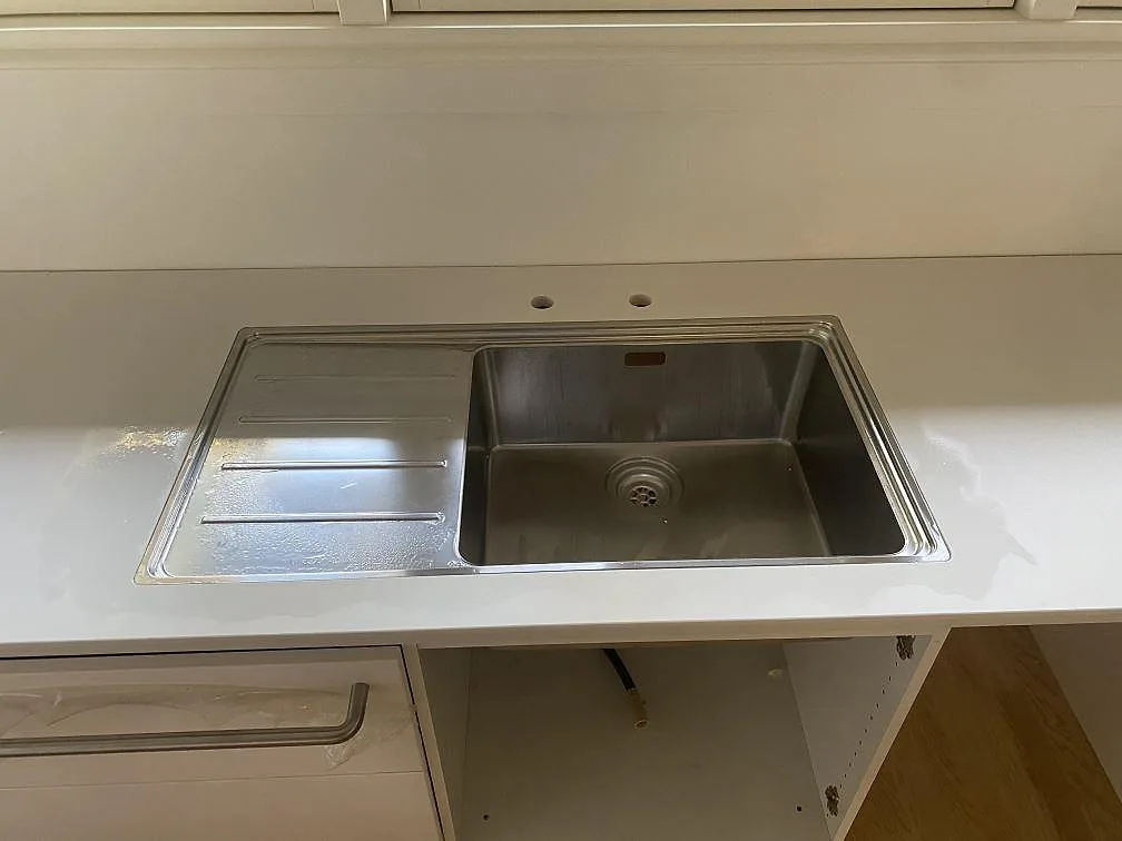 Närbild på rostfri diskho med avrinningsyta ovanpå en matt Dekton Zenith köksbänkskiva i Holte.