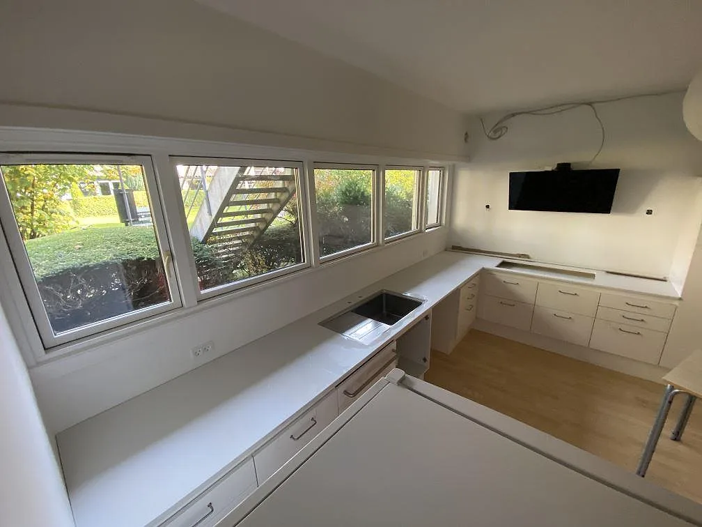 U-format kök i Holte med matt vit Dekton Zenith som köksbänkskiva längs fönstervägg och vita köksfronter.