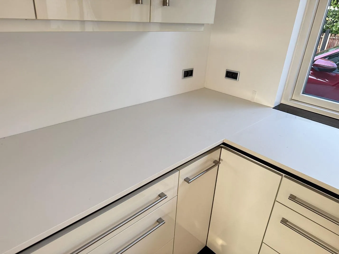 Köksbänkskiva i vit Dekton Zenith, matt keramik, med L-formad arbetsyta och fönsterläge i ett kök i Stenløse.