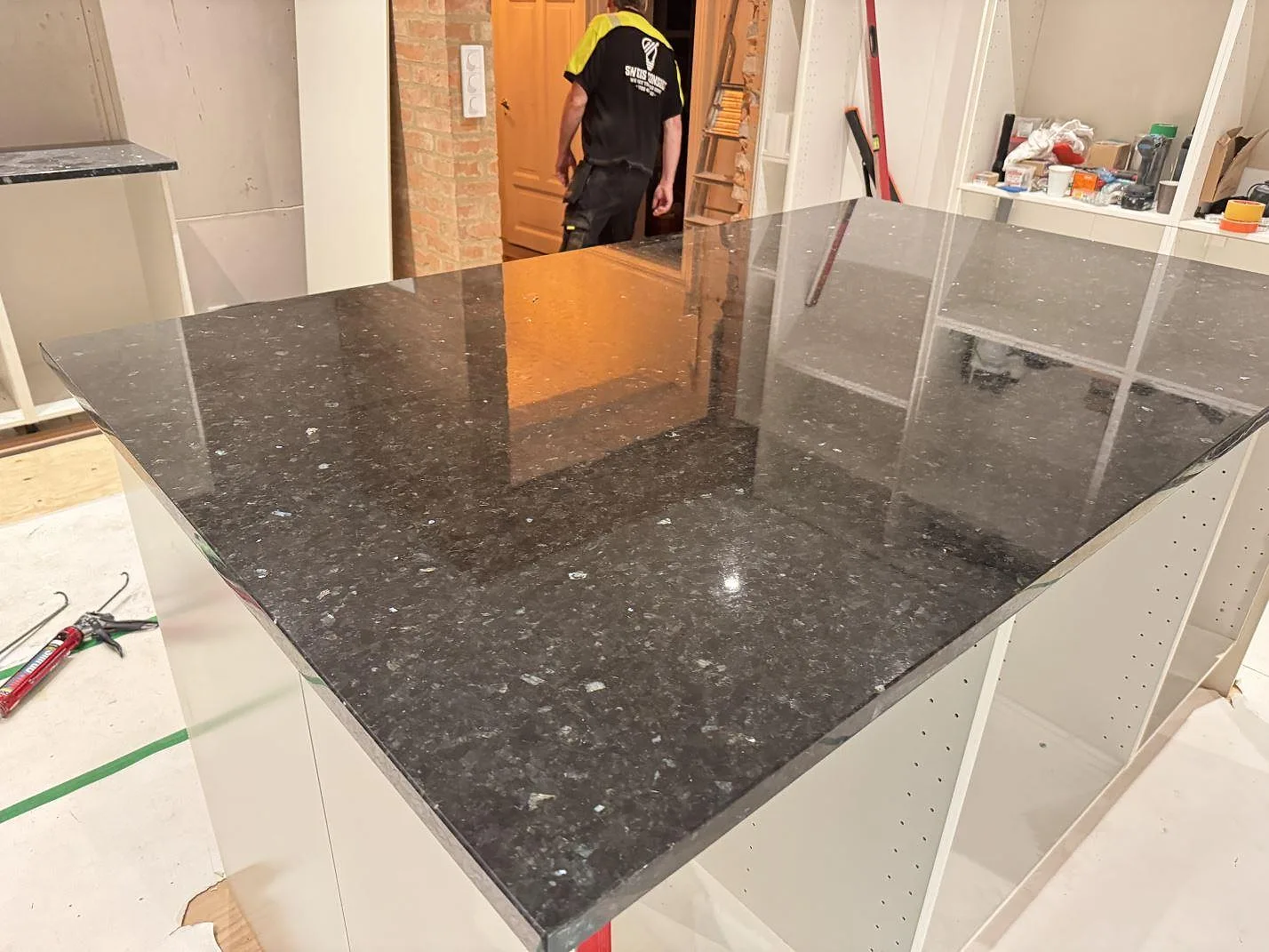 Stor köksö i polerad Emerald Pearl granit med öppna köksstommar och pågående montering i Genarp.