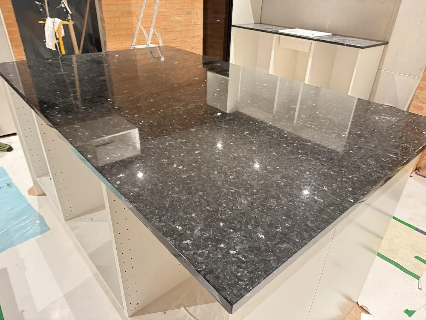 Närbild av polerad Emerald Pearl granit på köksö med väggbänk och vit ho i bakgrunden i Genarp.