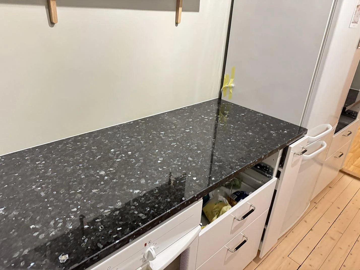 Rak köksbänkskiva i mörk polerad Emerald Pearl-granit med blågröna kristaller längs en vit skåpsrad i Göteborg.