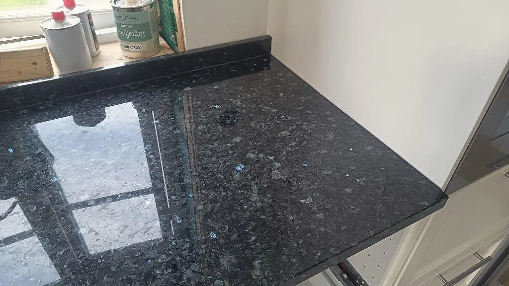 Närbild på polerad Emerald Pearl granit med blågröna pärlemorfält och låg stänkkant i Hönö.
