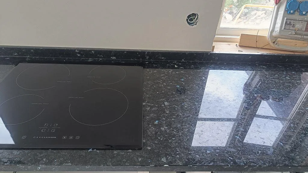 Köksbänkskiva i polerad Emerald Pearl granit med svart induktionshäll och fönsterreflexer i Hönö.