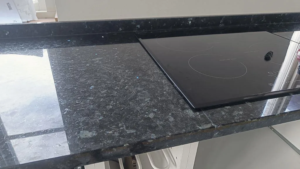 Detalj av blank Emerald Pearl granit med fasad kant och svart häll i köksmontering i Hönö.
